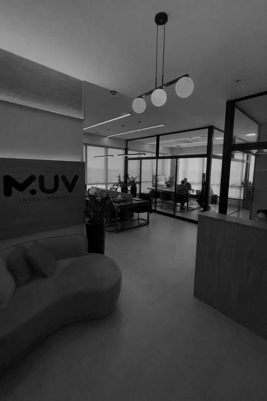 Recepção do escritório da MUV Investimentos com o logo na parede e a sala de reunião envidraçada ao fundo